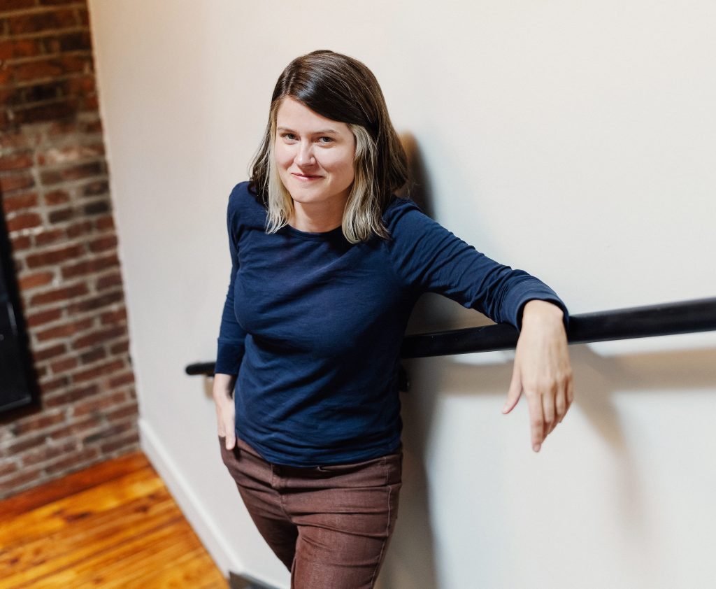 Photo of Christine Stroud; woman standing in stairwell, leaning on the railing. 